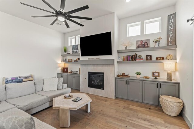 living area featuring a glass covered fireplace, a ceiling fan, and light wood-style floors