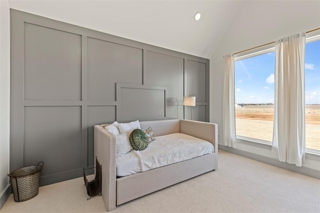 bedroom featuring lofted ceiling, multiple windows, light colored carpet, and a decorative wall