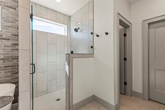 bathroom featuring baseboards, a freestanding tub, a tile shower, and tile patterned floors