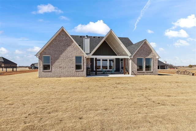 rear view of house featuring brick siding, a patio, a chimney, and a lawn