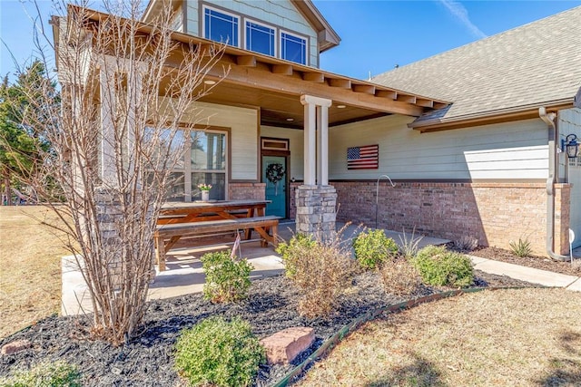 property entrance featuring covered porch, a shingled roof, and brick siding