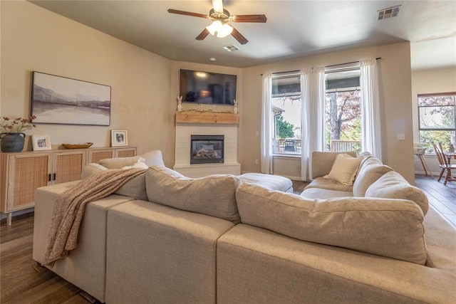 living room with ceiling fan, a glass covered fireplace, wood finished floors, and visible vents