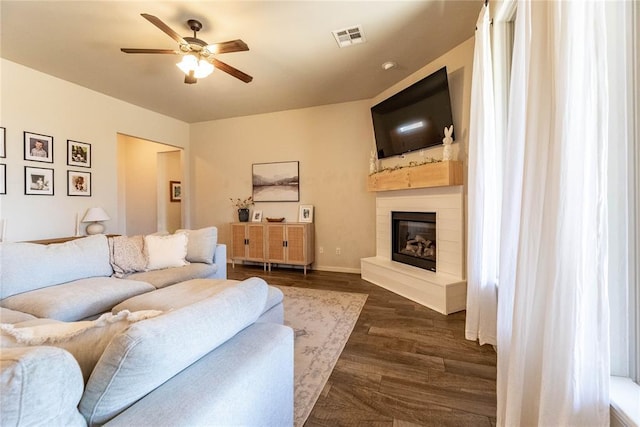 living room featuring baseboards, visible vents, a ceiling fan, a glass covered fireplace, and dark wood-type flooring