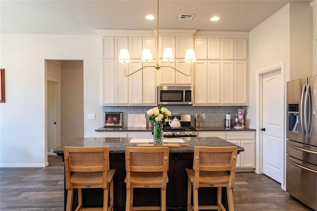 kitchen featuring visible vents, decorative backsplash, a kitchen island, appliances with stainless steel finishes, and dark wood-type flooring