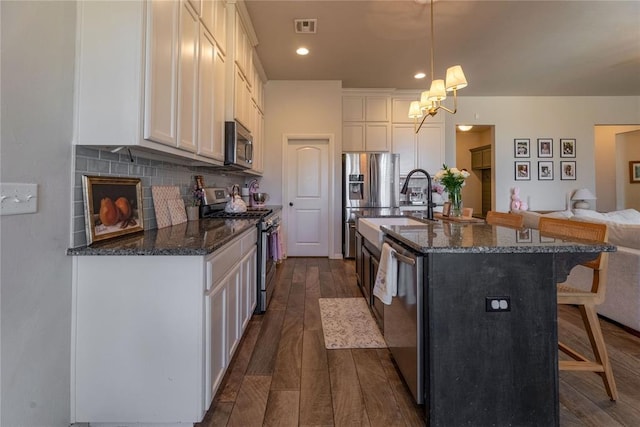 kitchen with a breakfast bar area, dark wood-type flooring, visible vents, appliances with stainless steel finishes, and tasteful backsplash