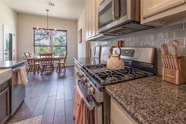 kitchen with dark wood-style flooring, stainless steel appliances, tasteful backsplash, visible vents, and dark stone countertops