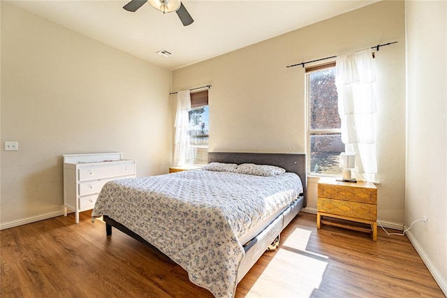 bedroom featuring visible vents, ceiling fan, baseboards, and wood finished floors