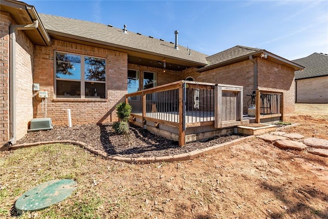 back of house featuring a shingled roof, brick siding, and a deck