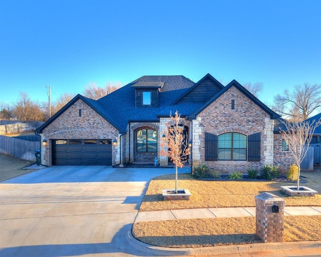 french provincial home with a garage, driveway, a shingled roof, and brick siding