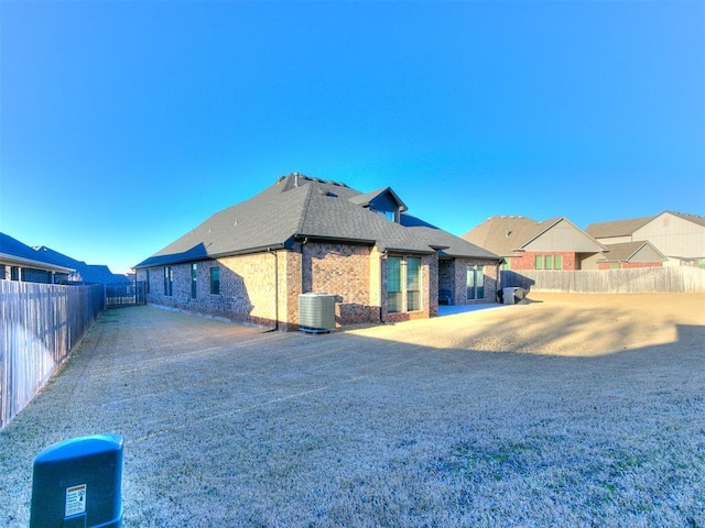 view of side of property with a shingled roof, central AC, brick siding, and a fenced backyard