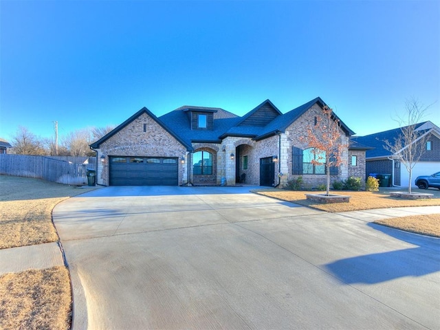 french provincial home with a garage, stone siding, driveway, and fence