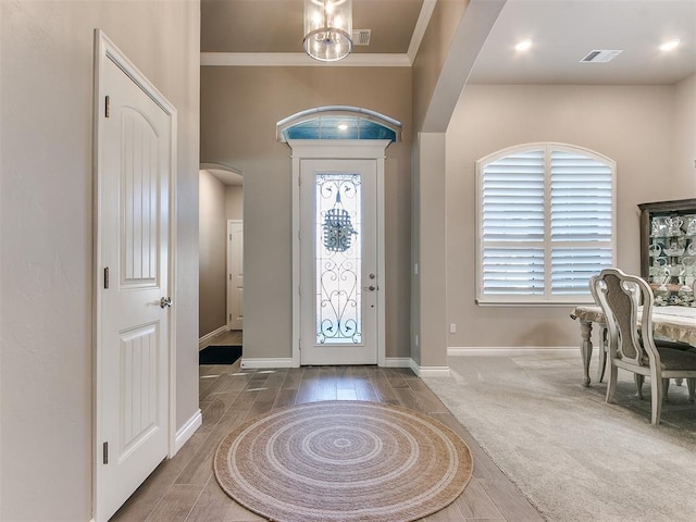 carpeted foyer entrance with arched walkways, crown molding, visible vents, and baseboards