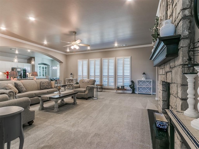 living area with arched walkways, light colored carpet, ceiling fan, ornamental molding, and a fireplace