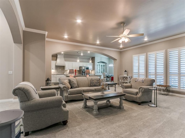 living room featuring arched walkways, ceiling fan, crown molding, and light colored carpet