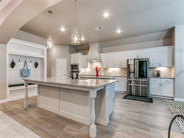 kitchen featuring visible vents, white cabinetry, appliances with stainless steel finishes, custom exhaust hood, and an island with sink