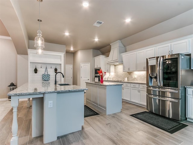 kitchen featuring a sink, visible vents, stainless steel refrigerator with ice dispenser, backsplash, and a center island with sink