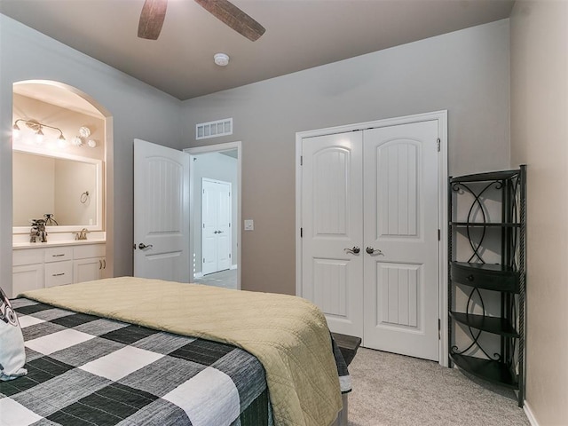 bedroom featuring a closet, visible vents, connected bathroom, light colored carpet, and a sink