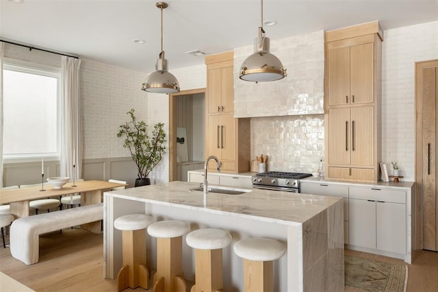 kitchen featuring light wood finished floors, an island with sink, wainscoting, gas stove, and a sink