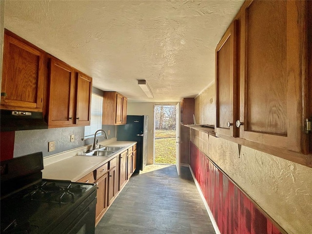 kitchen with a textured ceiling, under cabinet range hood, a sink, black gas stove, and light countertops