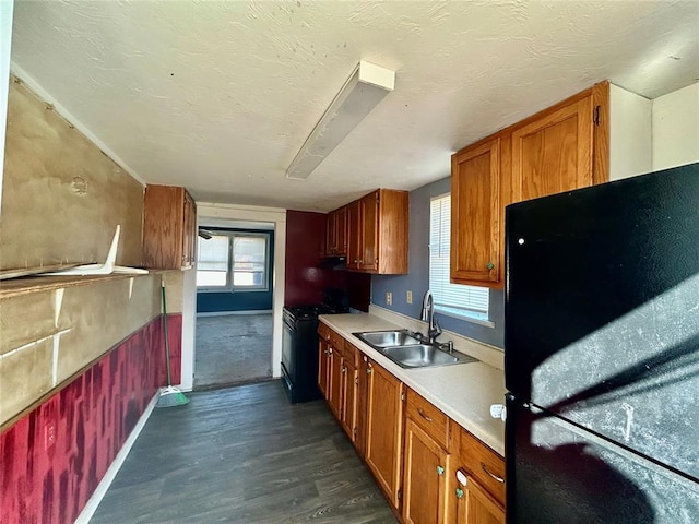 kitchen with brown cabinetry, dark wood-style flooring, light countertops, black appliances, and a sink