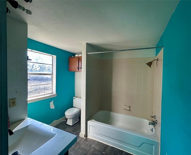 bathroom featuring baseboards, toilet, tub / shower combination, a textured ceiling, and a sink