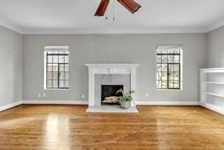 unfurnished living room with ornamental molding, a wealth of natural light, wood finished floors, and a high end fireplace