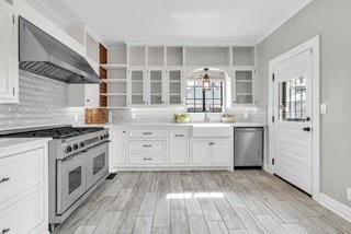 kitchen featuring open shelves, stainless steel appliances, decorative backsplash, white cabinetry, and wall chimney range hood