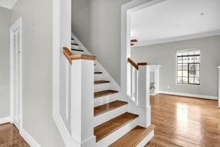 stairs featuring crown molding, baseboards, and wood finished floors