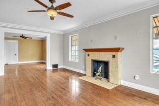 unfurnished living room featuring a fireplace, baseboards, crown molding, and wood finished floors