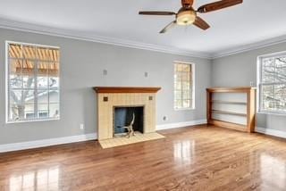 unfurnished living room featuring ornamental molding, a fireplace with flush hearth, ceiling fan, wood finished floors, and baseboards