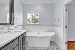 full bathroom with a freestanding tub, a wainscoted wall, crown molding, and vanity