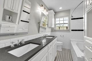 full bathroom with a tub to relax in, a sink, toilet, and tile walls