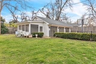 rear view of house featuring a sunroom, fence, and a lawn