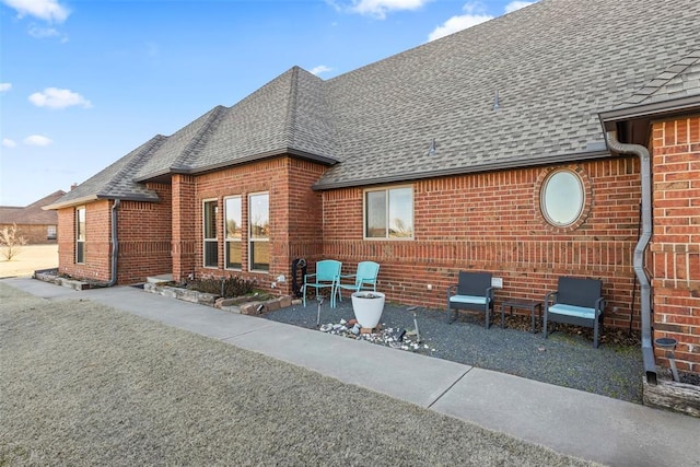 rear view of house featuring a shingled roof, brick siding, and a patio