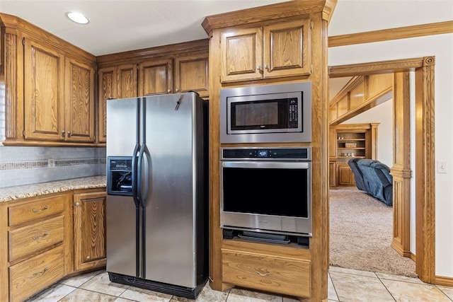 kitchen featuring light carpet, brown cabinets, stainless steel appliances, backsplash, and light tile patterned flooring