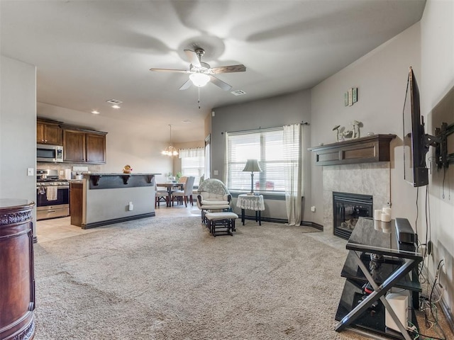 living area featuring light carpet, visible vents, baseboards, a tile fireplace, and ceiling fan with notable chandelier