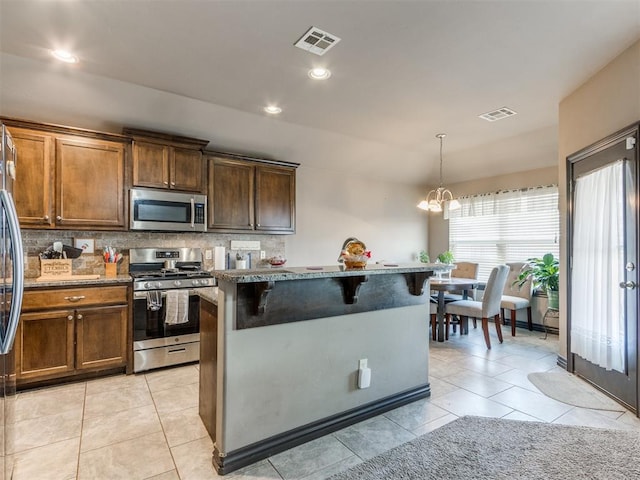 kitchen with visible vents, a breakfast bar area, stainless steel appliances, backsplash, and light tile patterned flooring