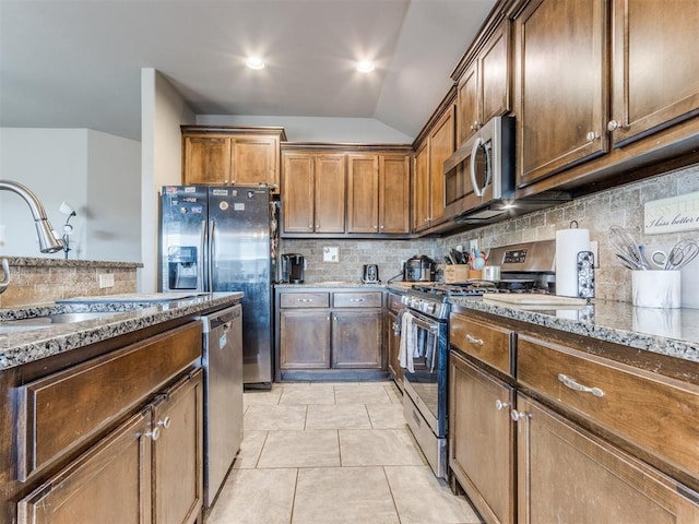 kitchen with light tile patterned floors, stone countertops, appliances with stainless steel finishes, a sink, and backsplash