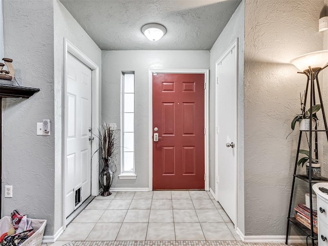 foyer entrance with a textured wall, a textured ceiling, baseboards, and light tile patterned floors