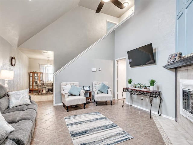 living area featuring light tile patterned floors, baseboards, a tile fireplace, high vaulted ceiling, and ceiling fan with notable chandelier