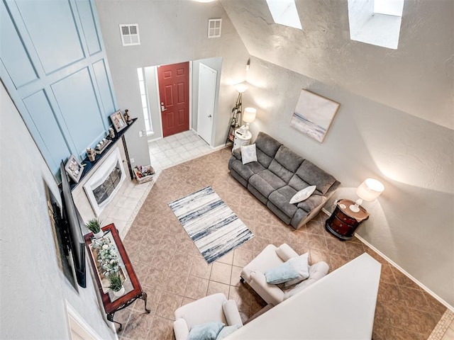 living room featuring high vaulted ceiling, a skylight, visible vents, and baseboards