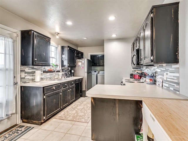 kitchen featuring black microwave, washer and clothes dryer, light countertops, and freestanding refrigerator