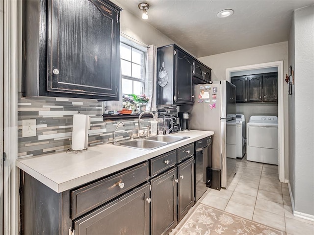 kitchen featuring light tile patterned floors, black dishwasher, decorative backsplash, washing machine and dryer, and a sink