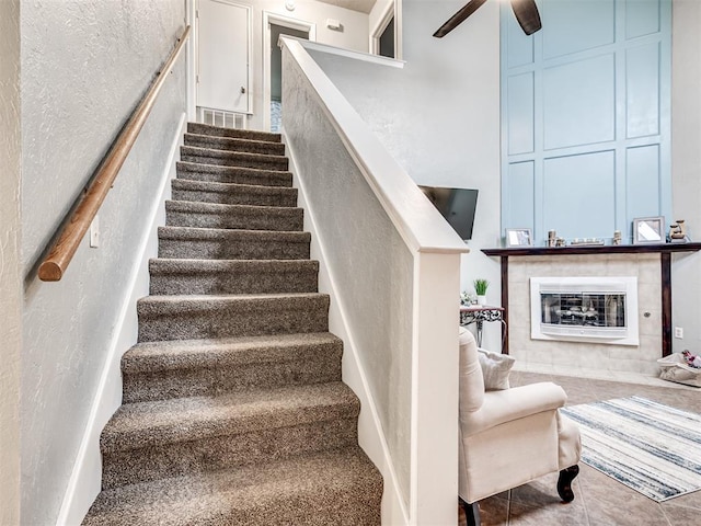 staircase with ceiling fan, a fireplace, and tile patterned flooring