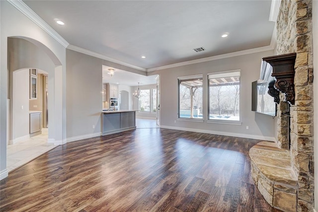 unfurnished living room with visible vents, arched walkways, wood finished floors, crown molding, and a stone fireplace