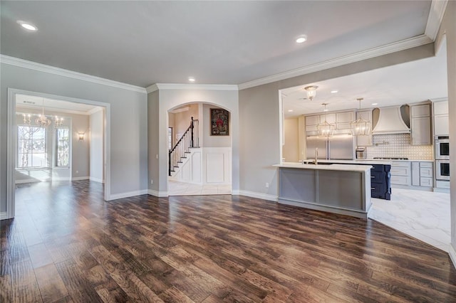 unfurnished living room featuring arched walkways, dark wood-style floors, a notable chandelier, stairs, and a sink