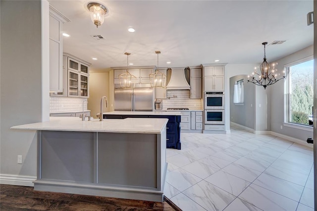 kitchen with hanging light fixtures, premium range hood, light countertops, and glass insert cabinets