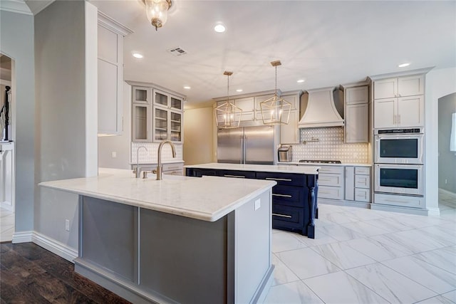 kitchen featuring appliances with stainless steel finishes, glass insert cabinets, a peninsula, premium range hood, and pendant lighting