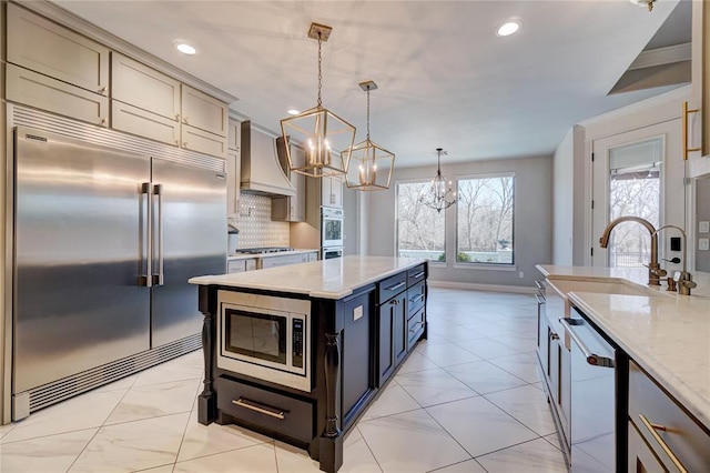 kitchen with built in appliances, a kitchen island, a sink, custom exhaust hood, and decorative light fixtures