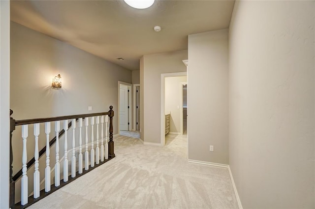 hall featuring light carpet, an upstairs landing, and baseboards